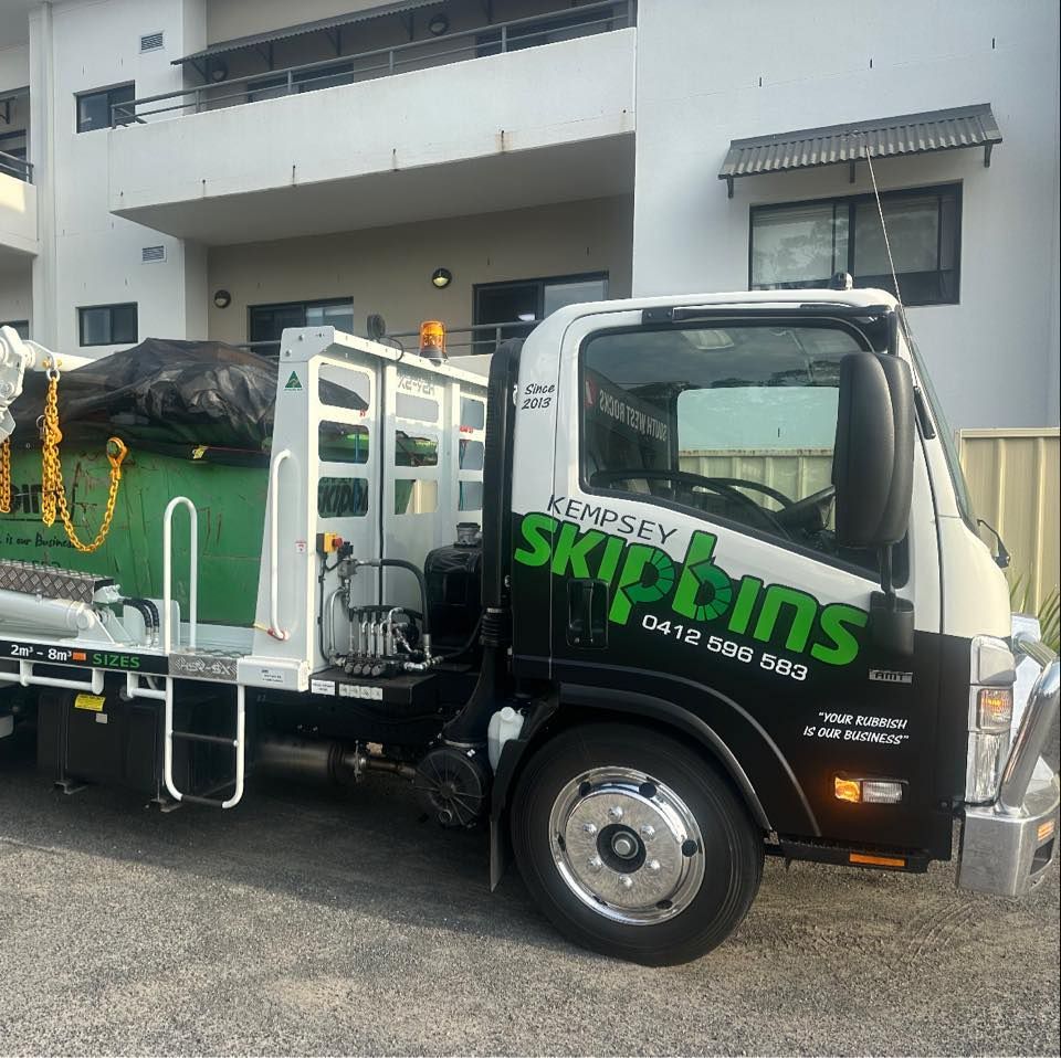 A Parked White Flatbed Truck Carrying A Green Skip Bin — Kempsey Skip Bins In South West Rocks, NSW