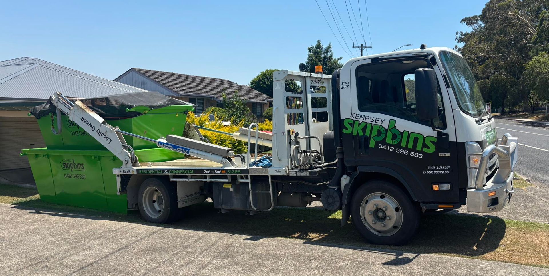 A Green Skip Bin Being Loaded onto A Skip Truck on A Driveway — Kempsey Skip Bins In Hat Head, NSW