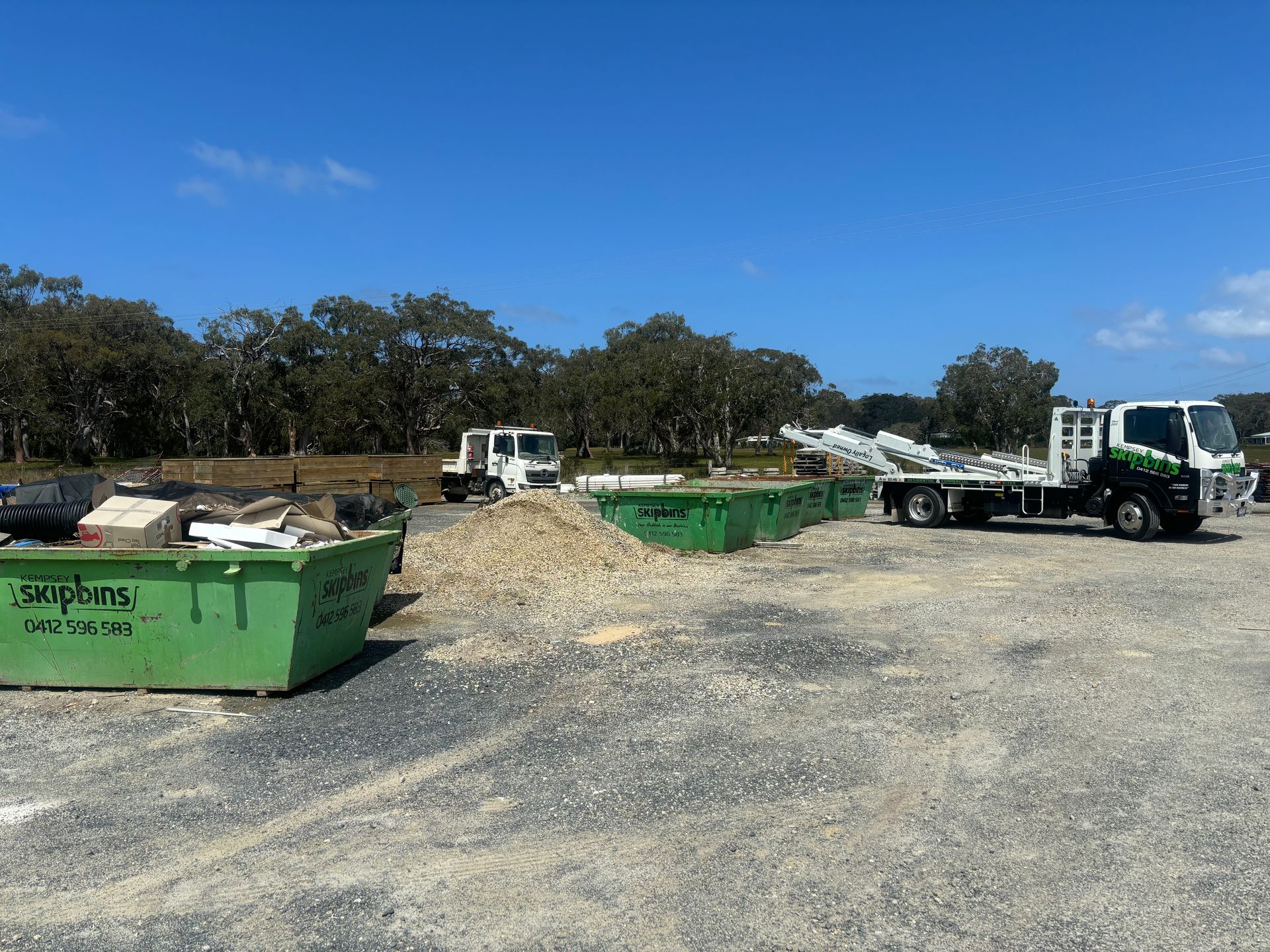 Green Bins and Trucks Filled with Debris in An Outdoor Gravel — Kempsey Skip Bins In Willawarrin, NSW