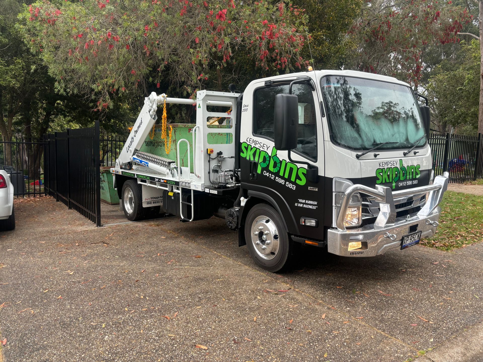 A Green Skip Bin Sitting Behind A Parked White Truck — Kempsey Skip Bins In Stuarts Point, NSW