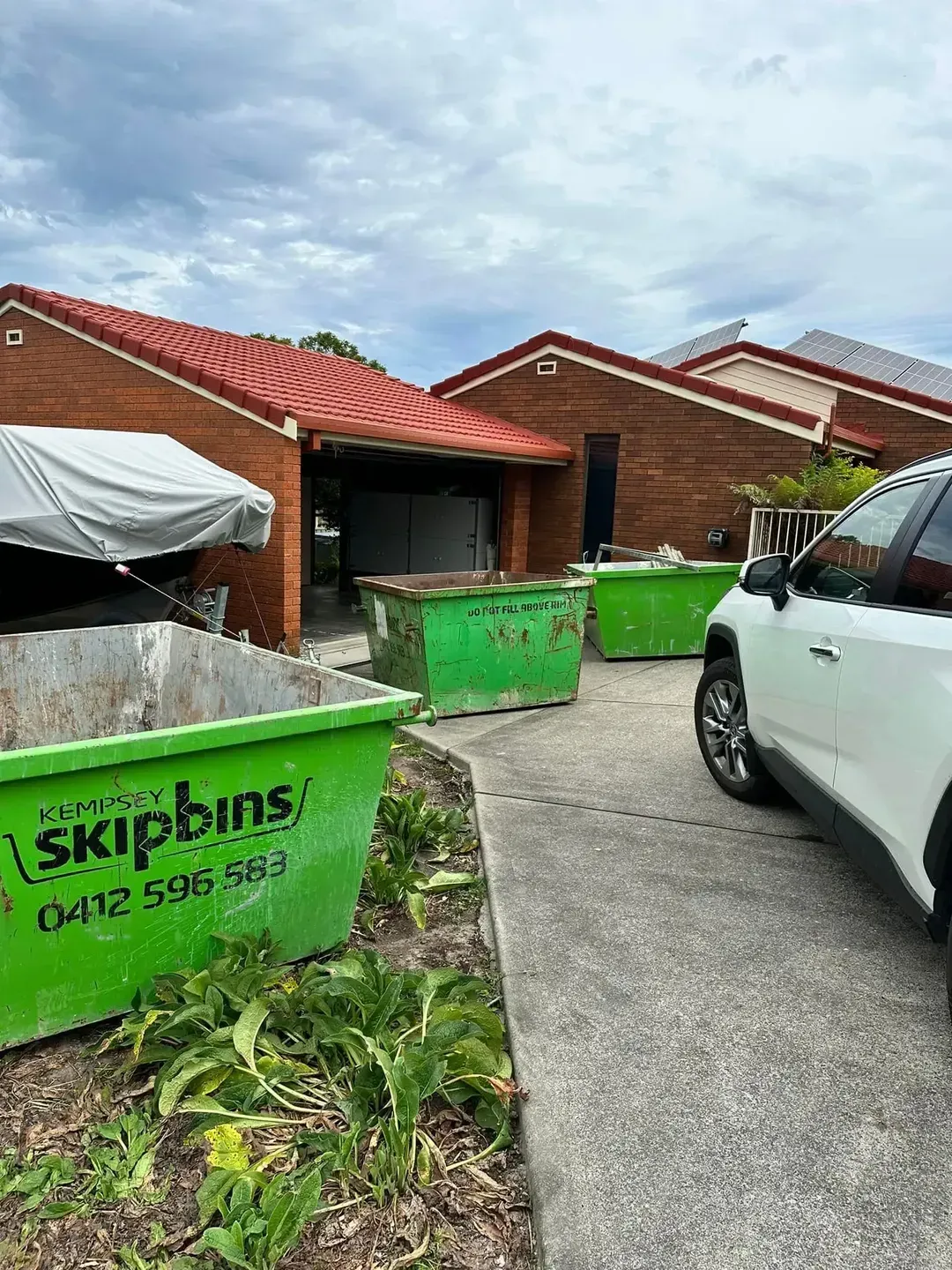 Three Green Skip Bins Outside a Brick House — Kempsey Skip Bins In Gladstone, QLD