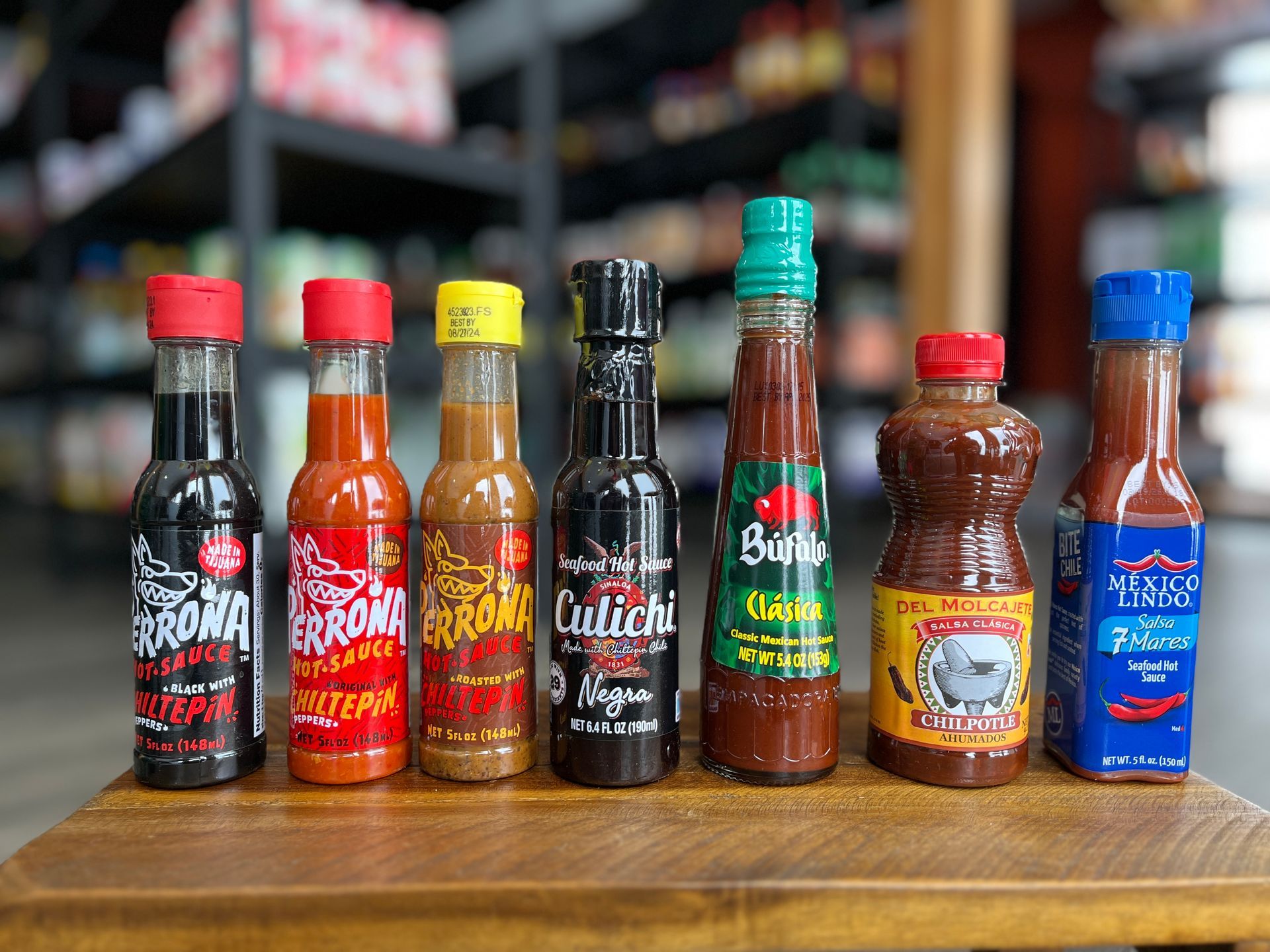 A variety of hot sauces are lined up on a wooden table.