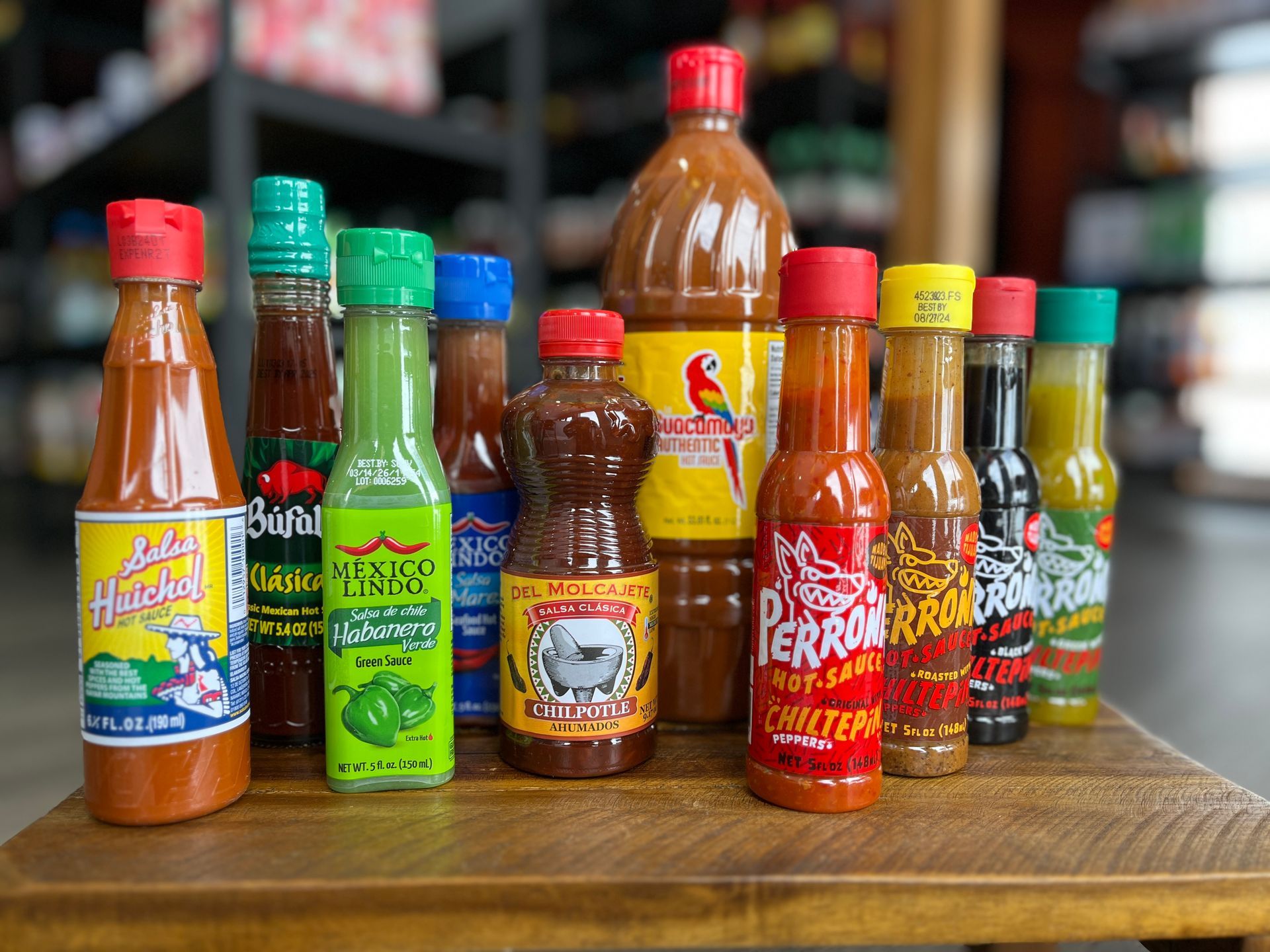 A variety of hot sauces are sitting on a wooden table.