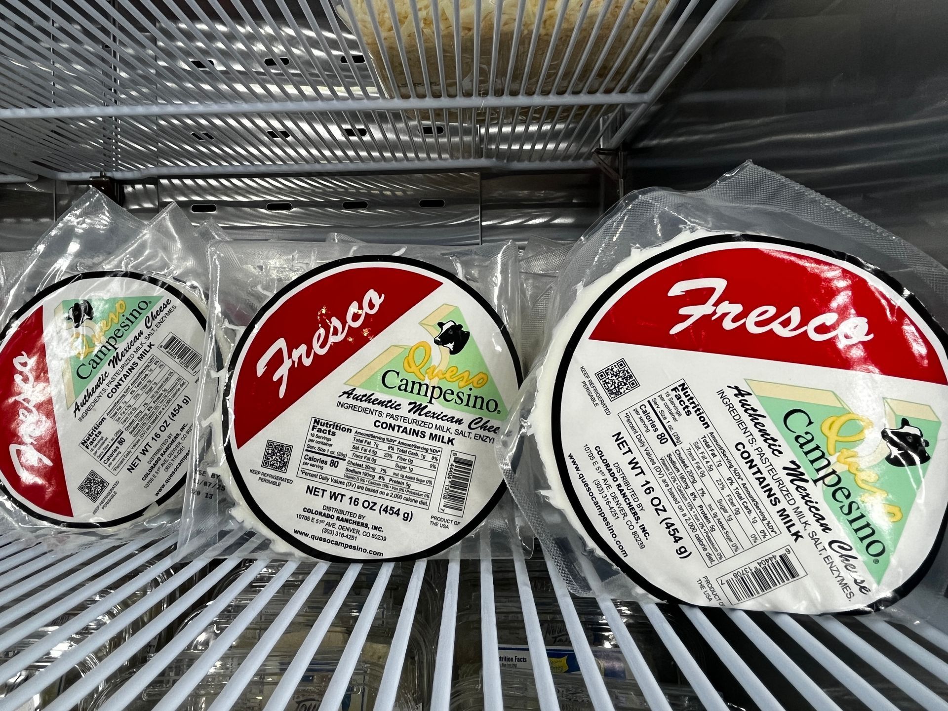 Three packages of cheese are sitting on a shelf in a refrigerator.