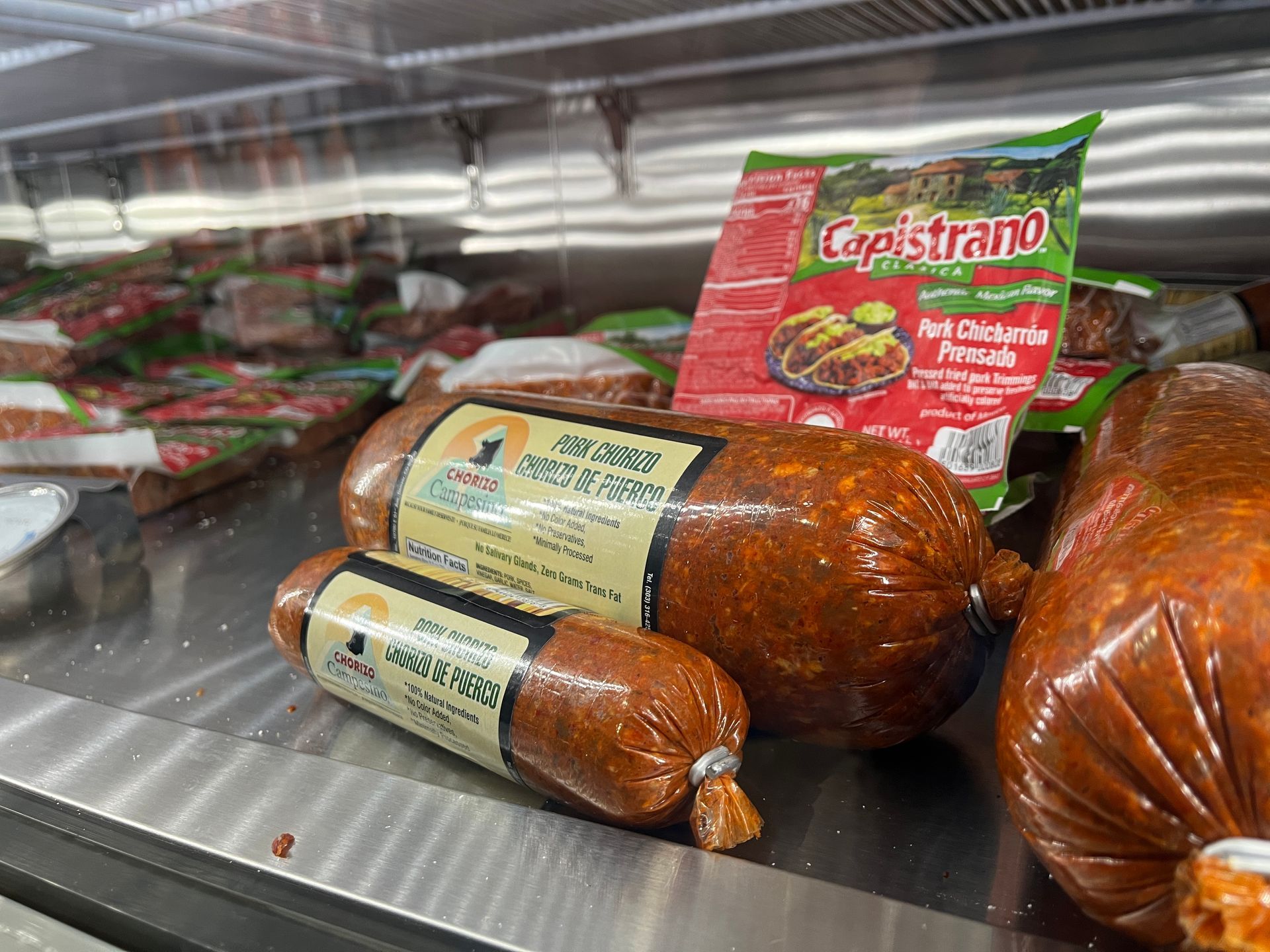 A bunch of sausages are sitting on a shelf in a refrigerator.