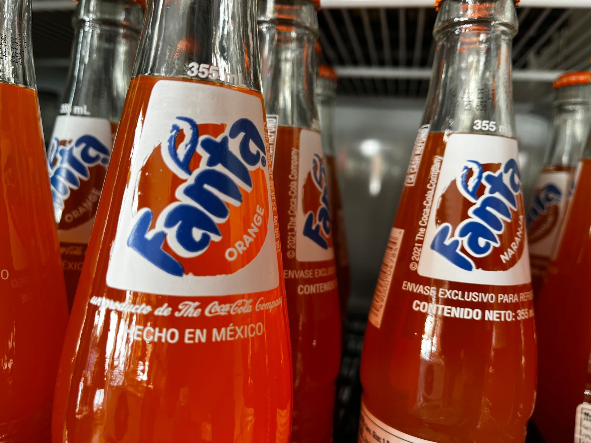 Several bottles of fanta orange soda are lined up on a shelf
