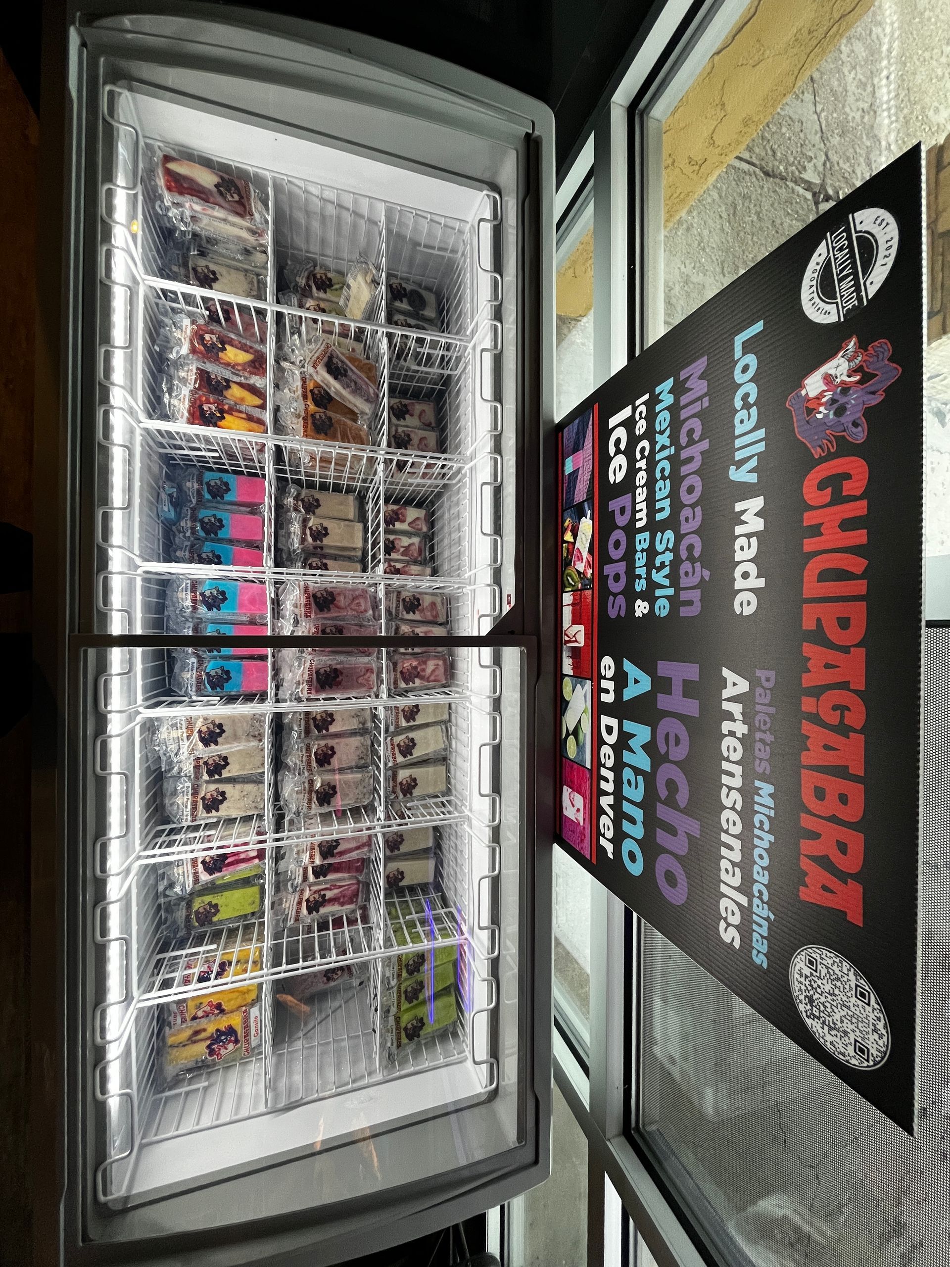 A refrigerator filled with ice pops and a sign that says locally made