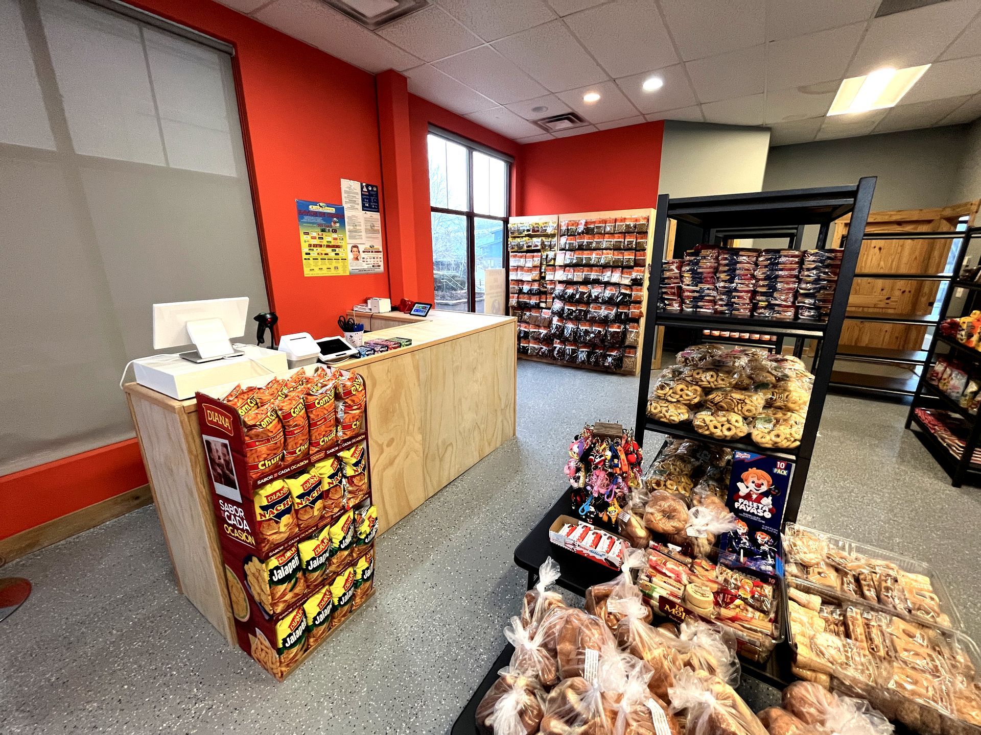Interior of a small convenience store with snacks, shelves of products, and a wooden counter with a point of sale system.