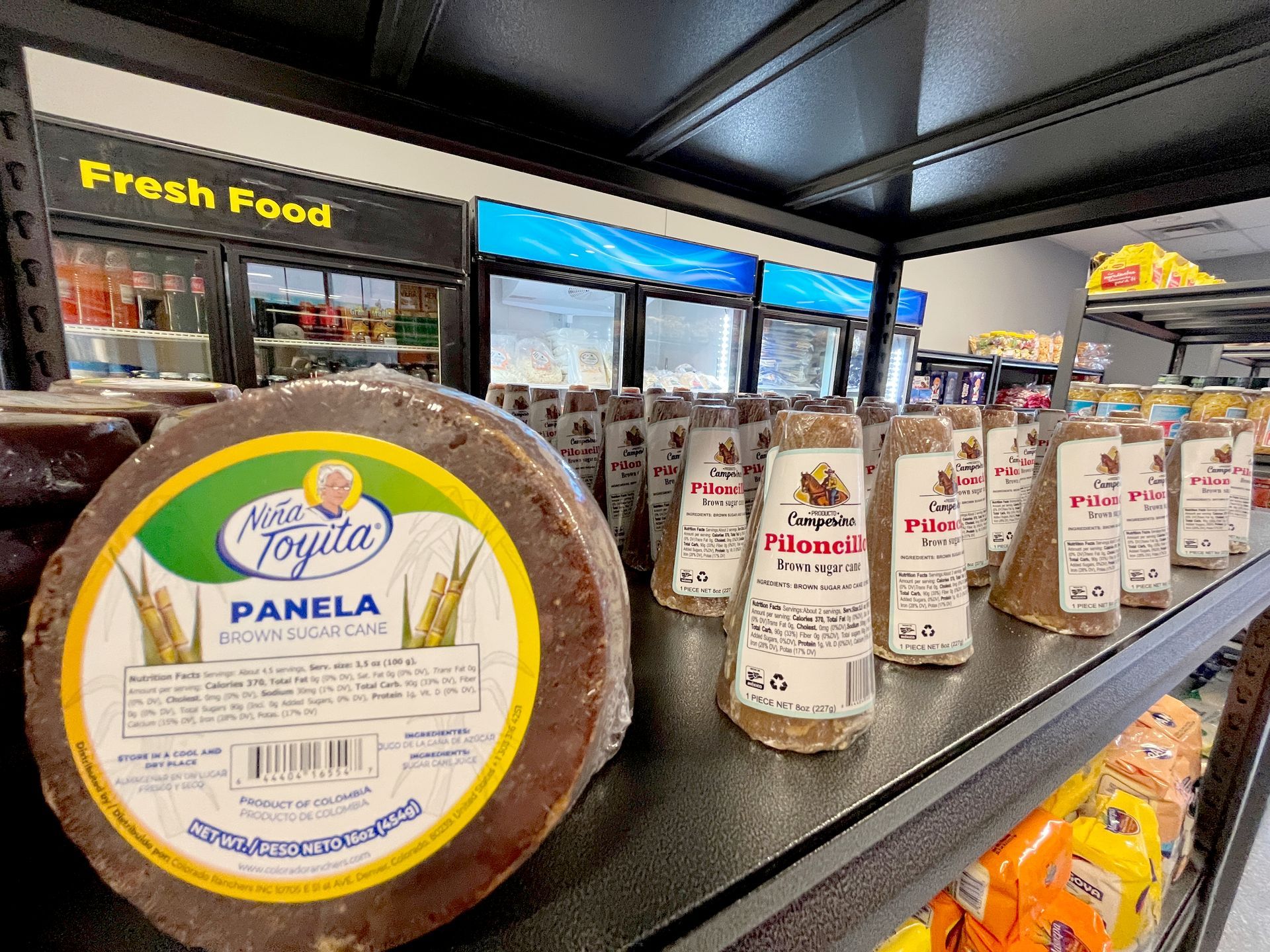 Shelves of panela sugar rounds and blocks in a store. Coolers in background.