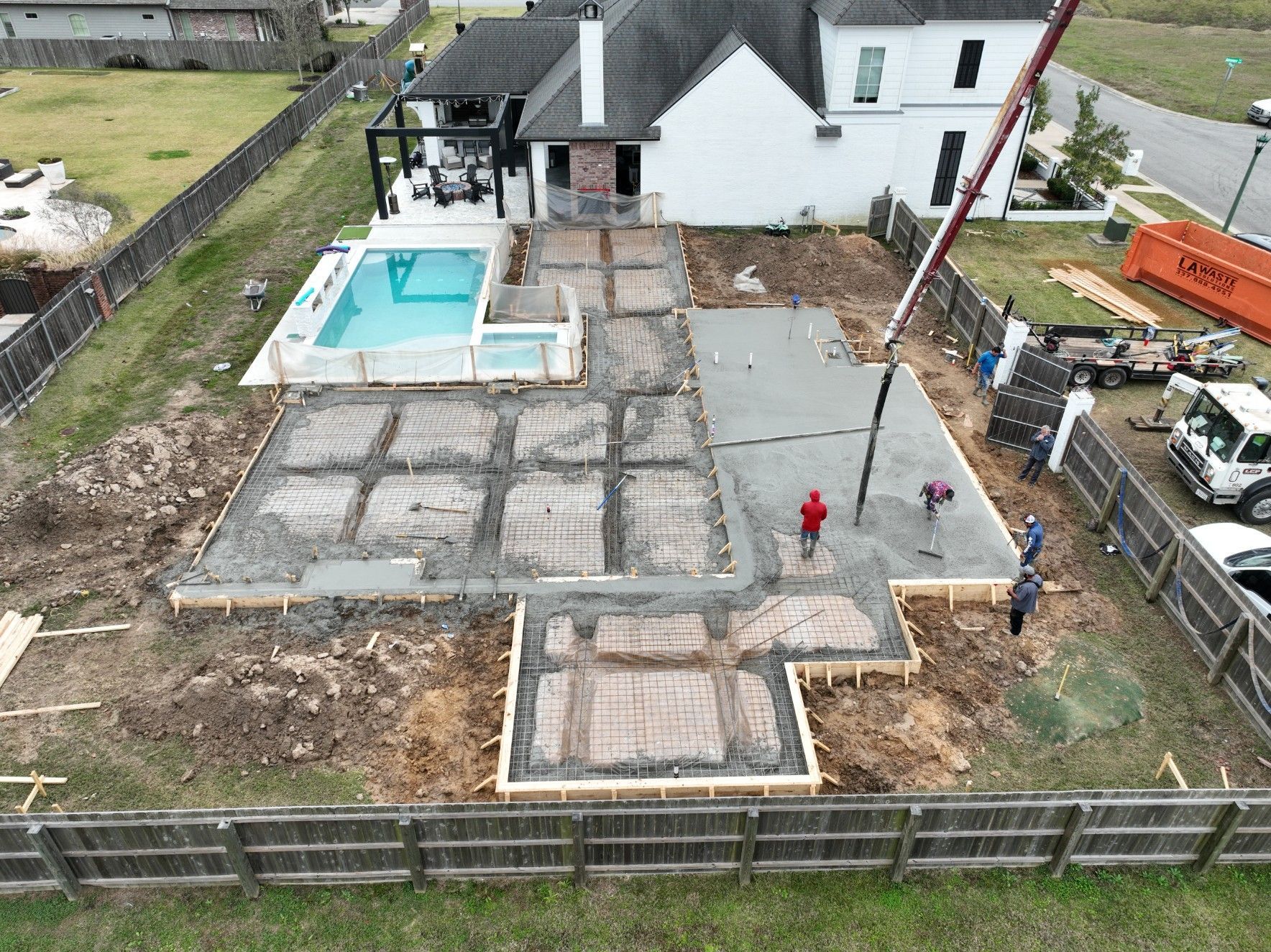 Construction site: pouring concrete patio next to a house with a pool.