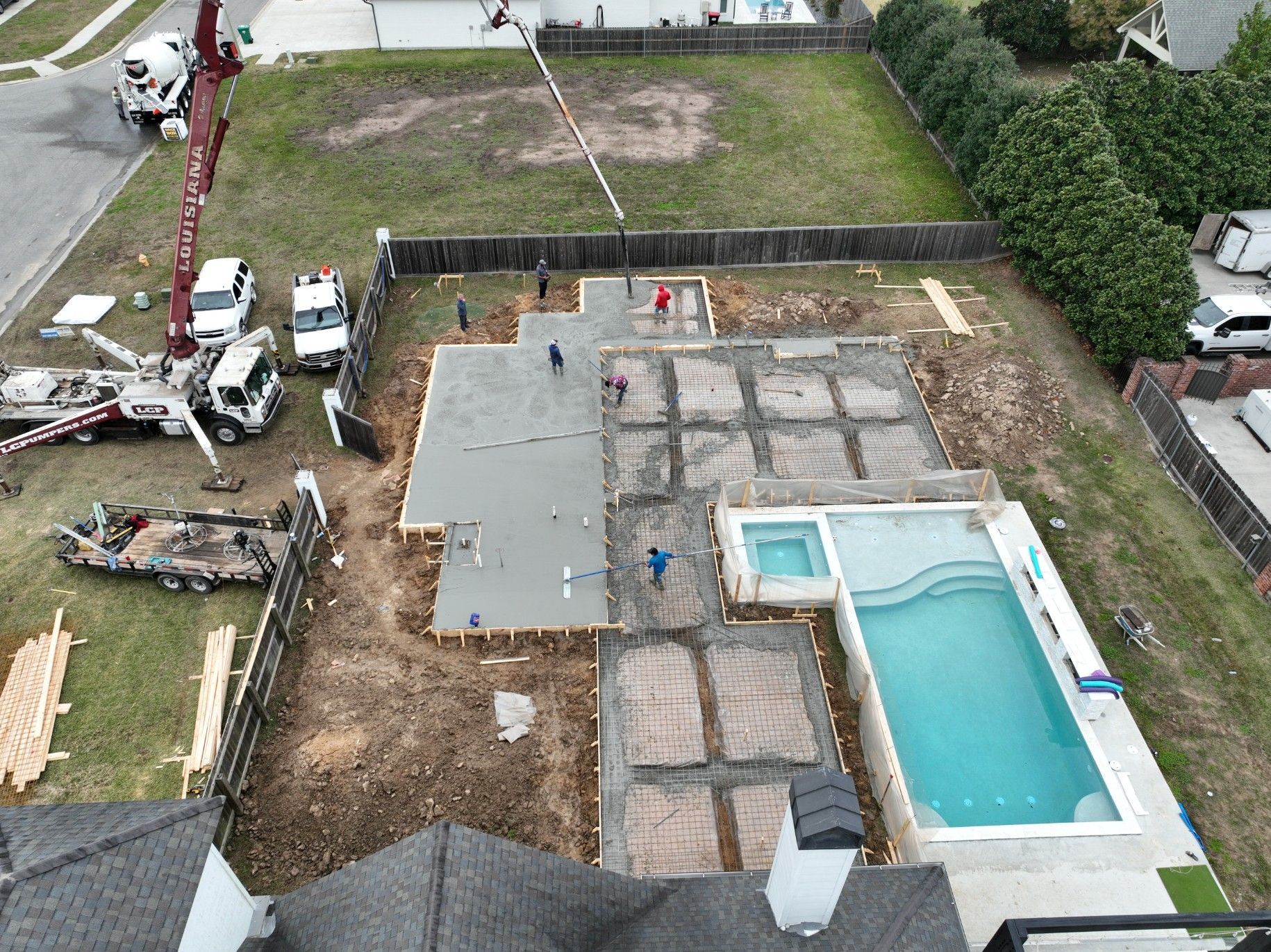 Aerial view of concrete foundation being poured for a home with a pool and construction equipment.