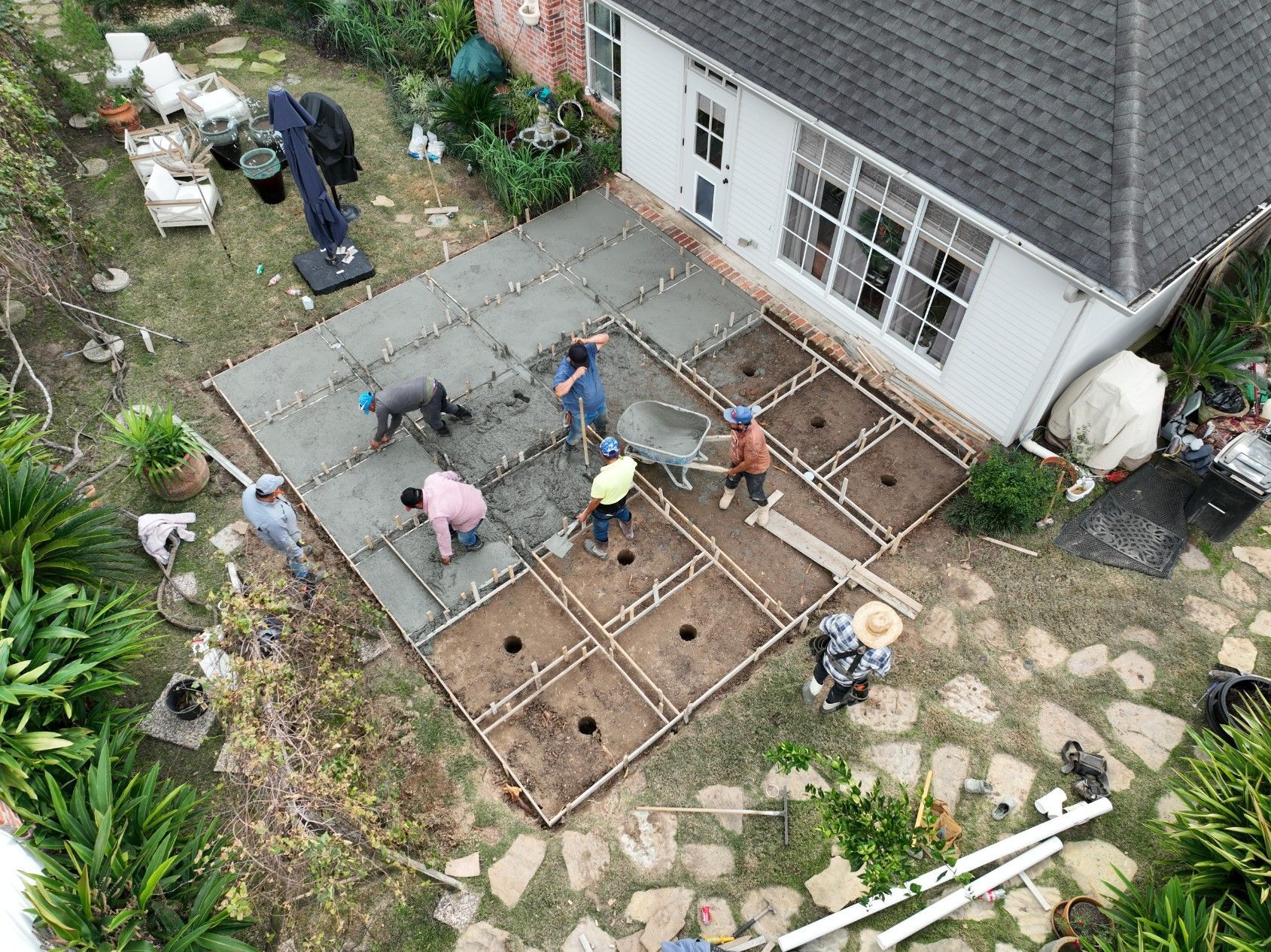 Concrete patio being poured in a backyard; several workers, a dog, and house visible.