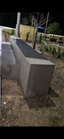 A long, gray concrete bench in a park setting at night.