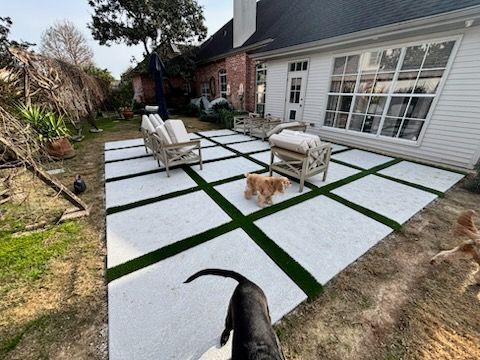 Backyard patio with white squares and green turf insets; two dogs, seating, and a house.
