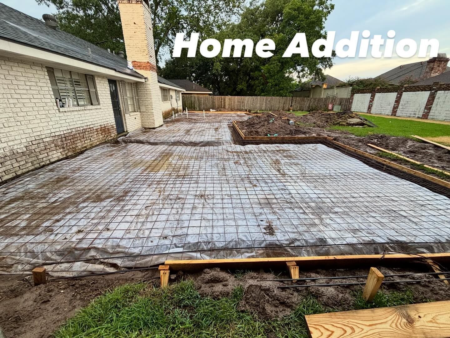 Construction site for a home addition, with prepared concrete foundation, rebar grid, and surrounding dirt.