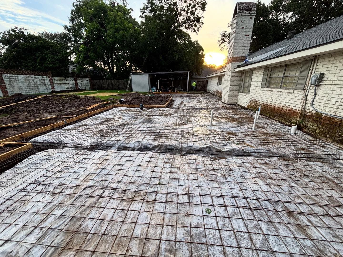 Overhead view of a sunlit backyard construction site, with exposed wooden shingles and a brick house.