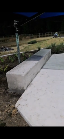Concrete bench and slab in an outdoor setting, with a dark sky and vegetation in the background.
