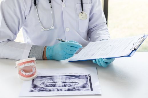 A Dentist Is Sitting At A Desk Looking At A Clipboard — Miami Denture Clinic In Burleigh Heads, QLD