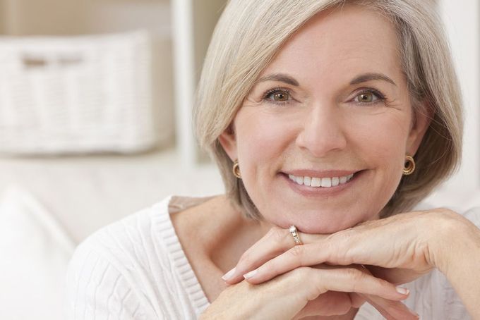 An Older Woman Is Smiling With Her Hands On Her Face — Miami Denture Clinic In Burleigh Heads, QLD