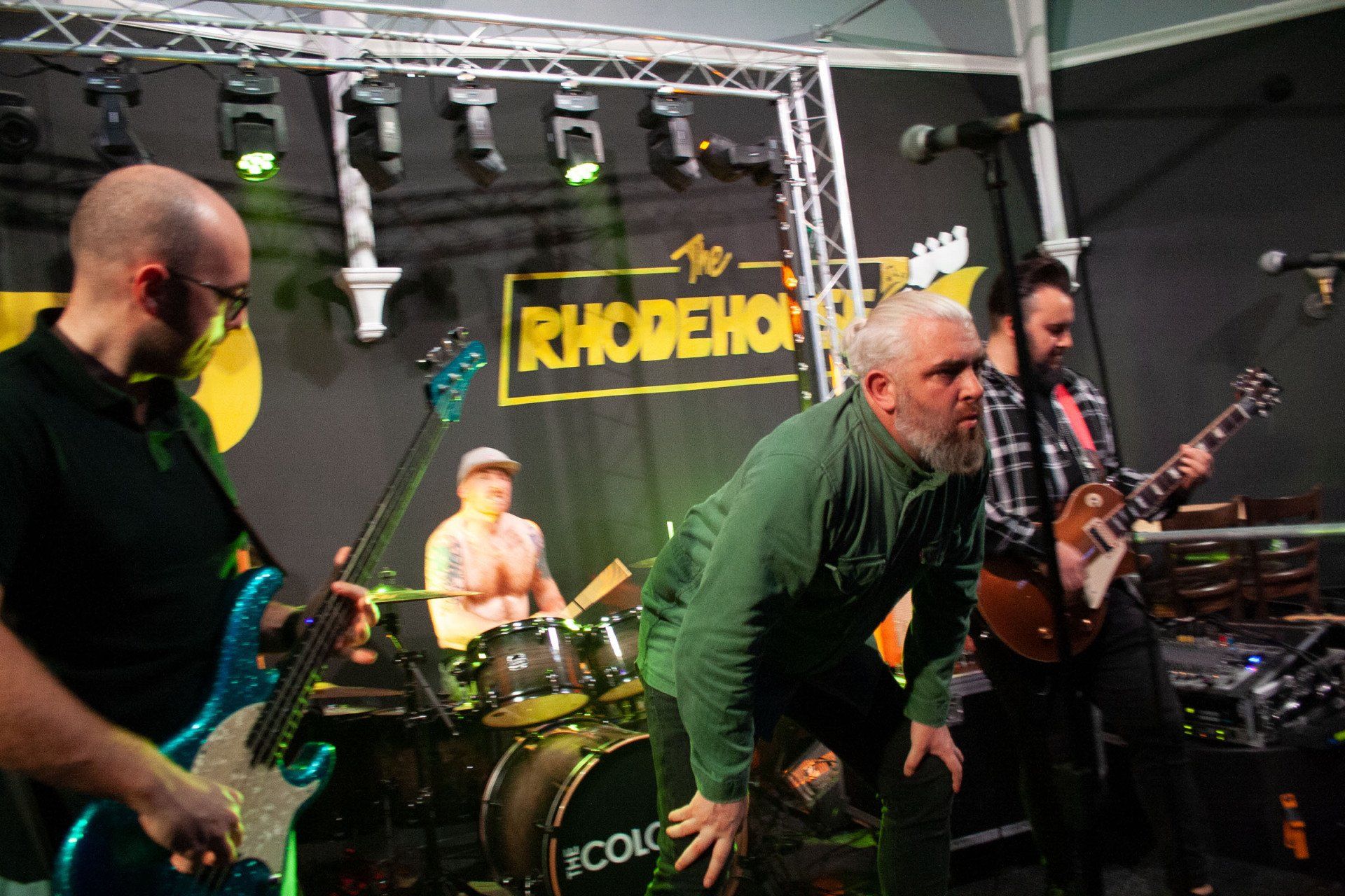 A group of men are playing instruments on a stage in front of a sign that says rhodehouse