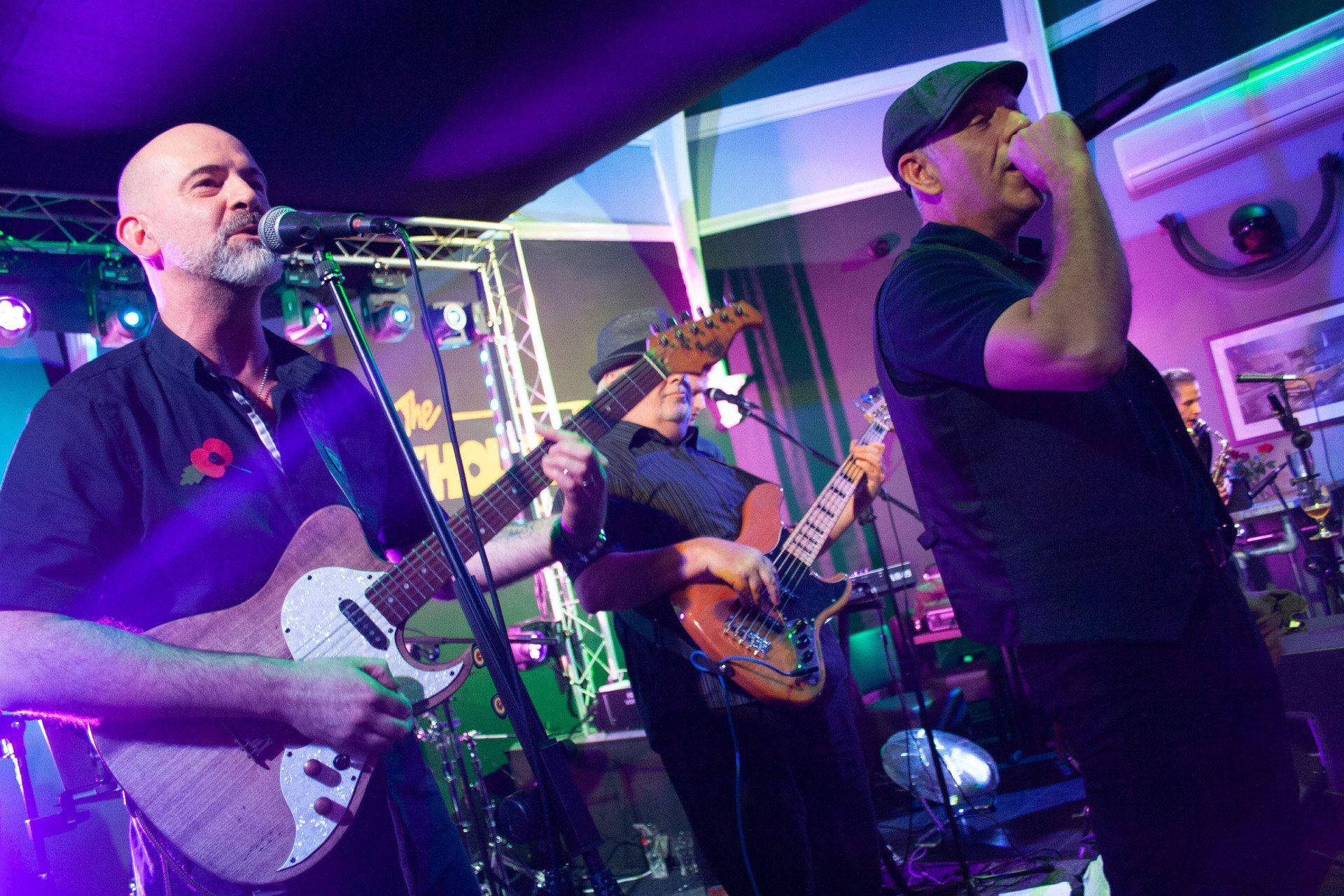 A group of men are playing guitars and singing into microphones on a stage at the rhodehouse
