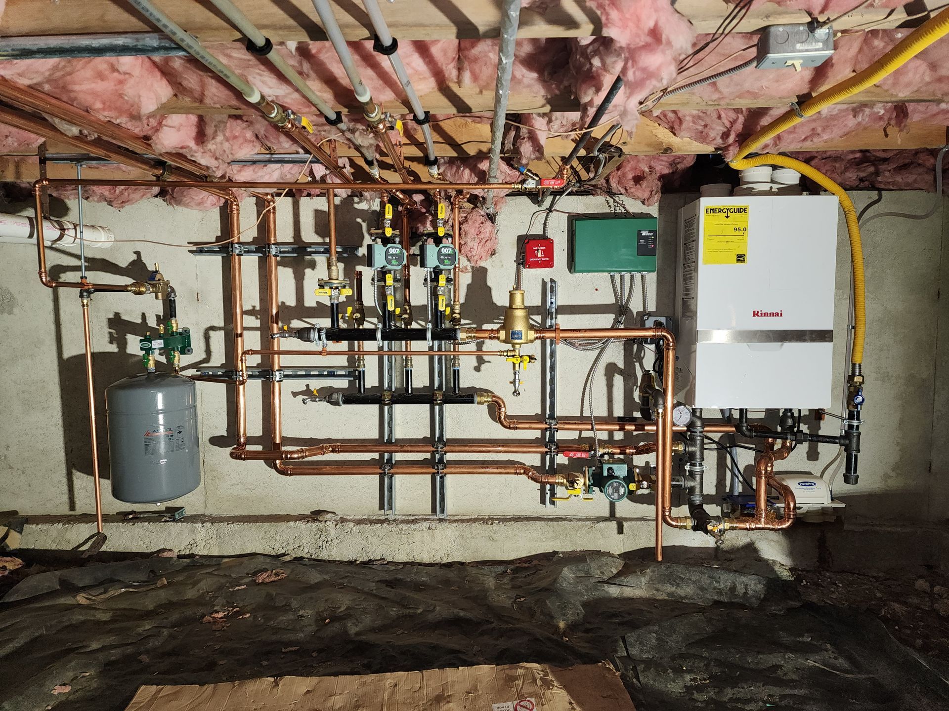 Copper pipes and boiler in a basement setting, with various valves and an expansion tank.
