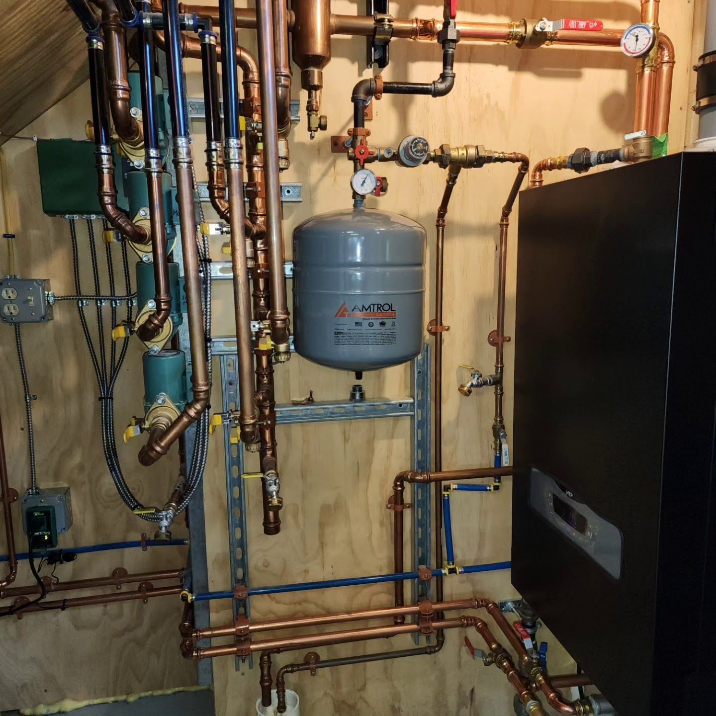Copper pipes and a grey expansion tank mounted on a wooden wall, part of a heating system.