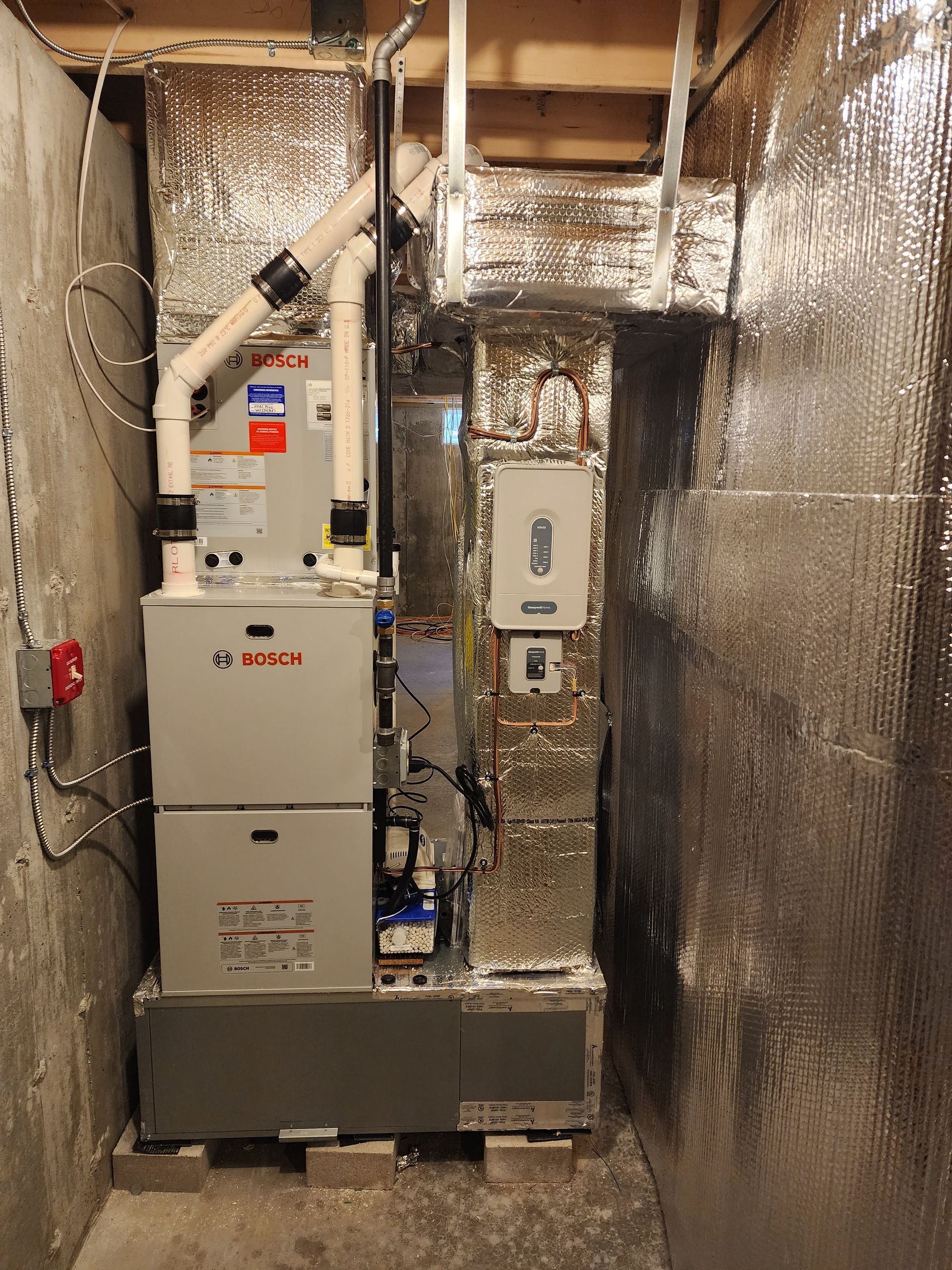 HVAC system installed in a basement, with silver insulated walls. A Bosch furnace unit sits on blocks.