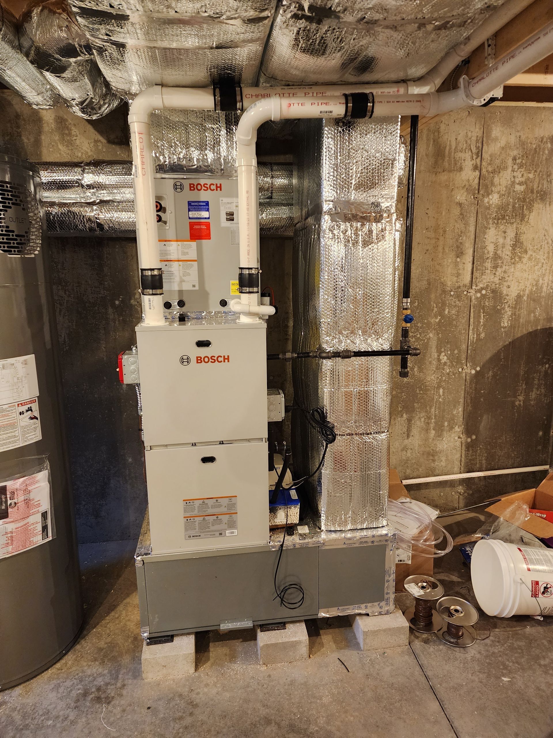 A gas furnace with white pipes installed in a basement next to a water heater.
