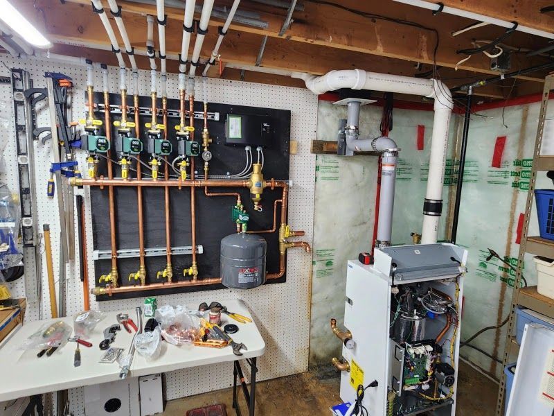 Hydronic heating system installation in a basement. Copper pipes, green pumps, and a white boiler.