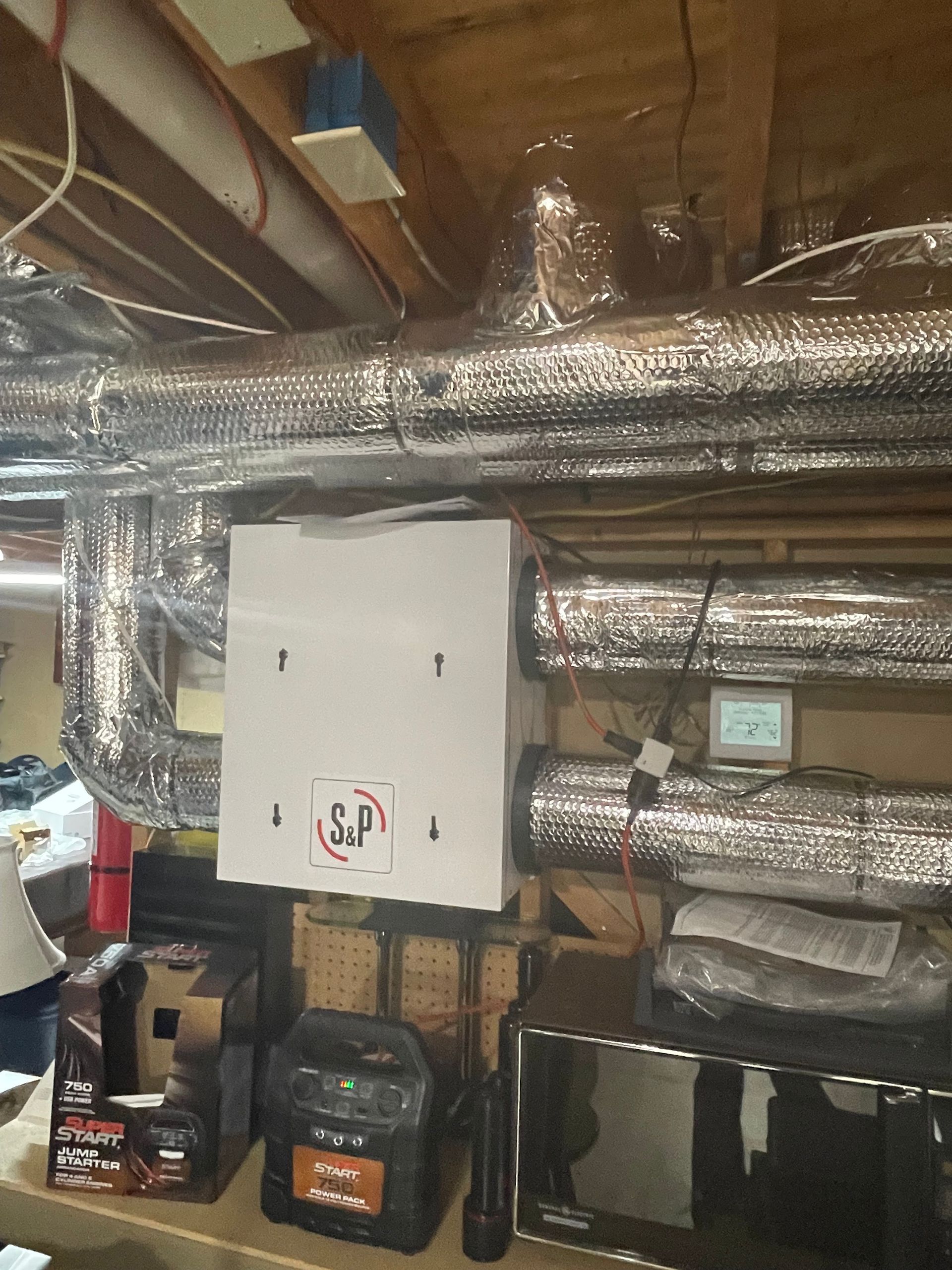 White HVAC unit in basement with silver ductwork and control panel.