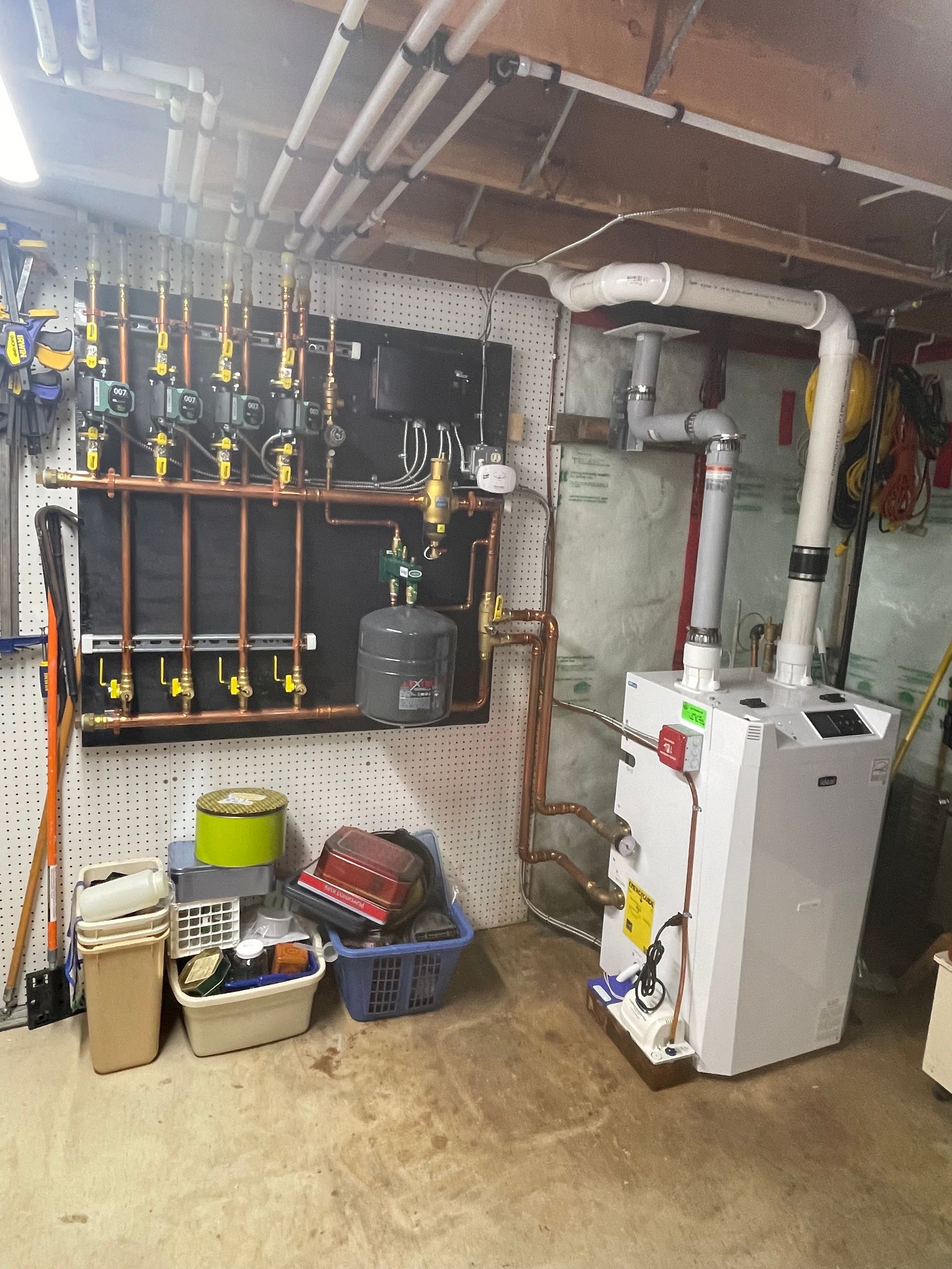 Basement with a white furnace, copper pipes, and a black control panel on a pegboard.