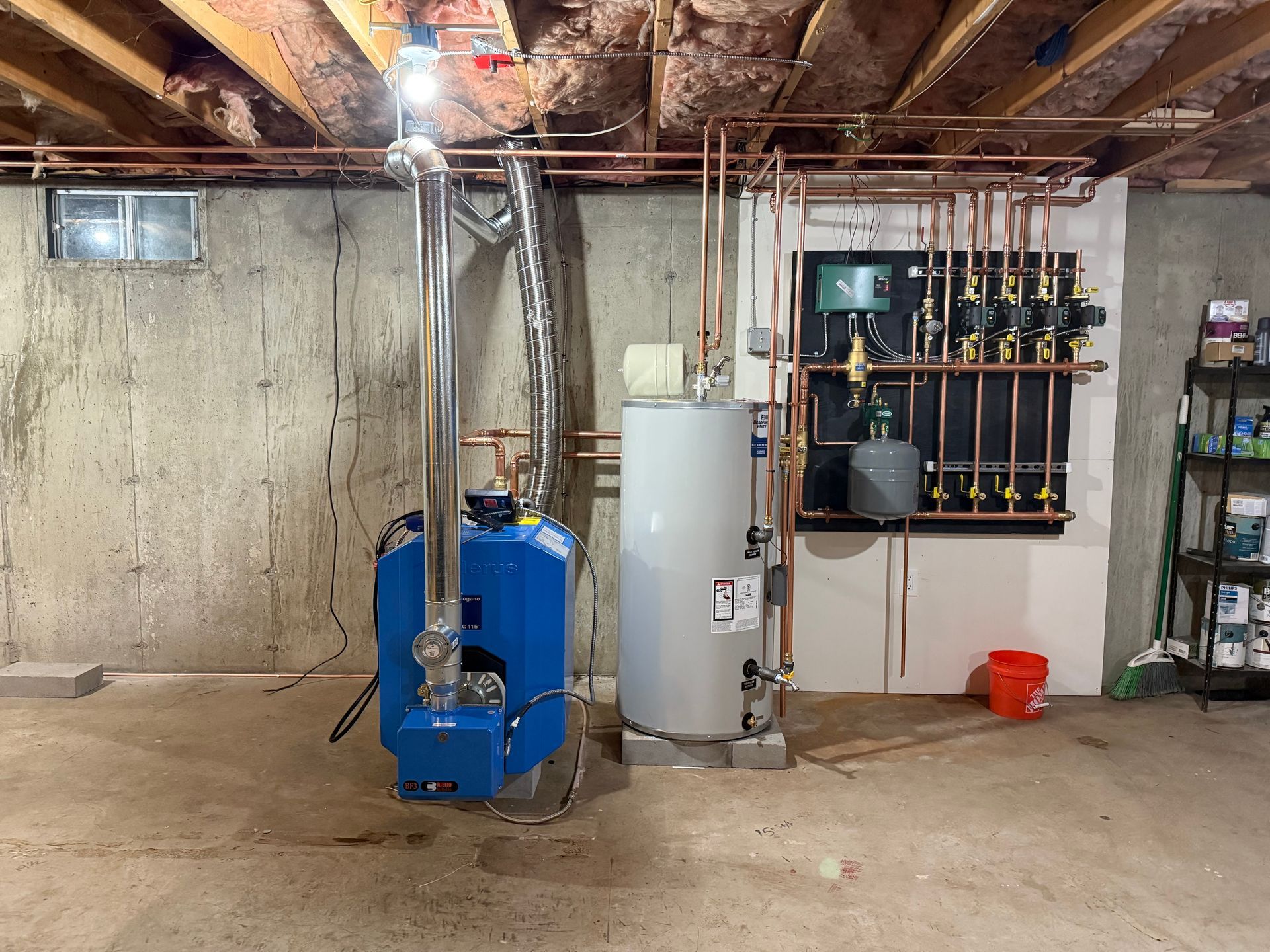 Blue boiler and water heater in a basement, with copper pipes along the wall.