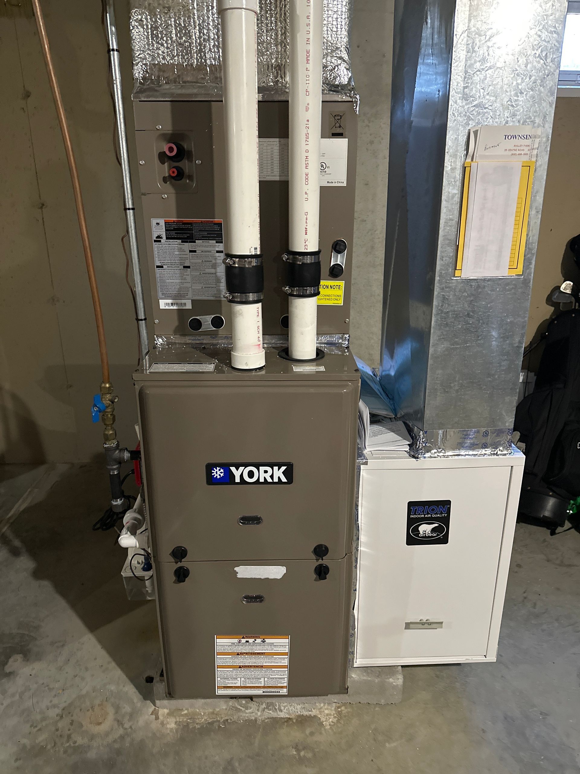 York furnace with white PVC pipes, vent ductwork, and an air filter in a basement.