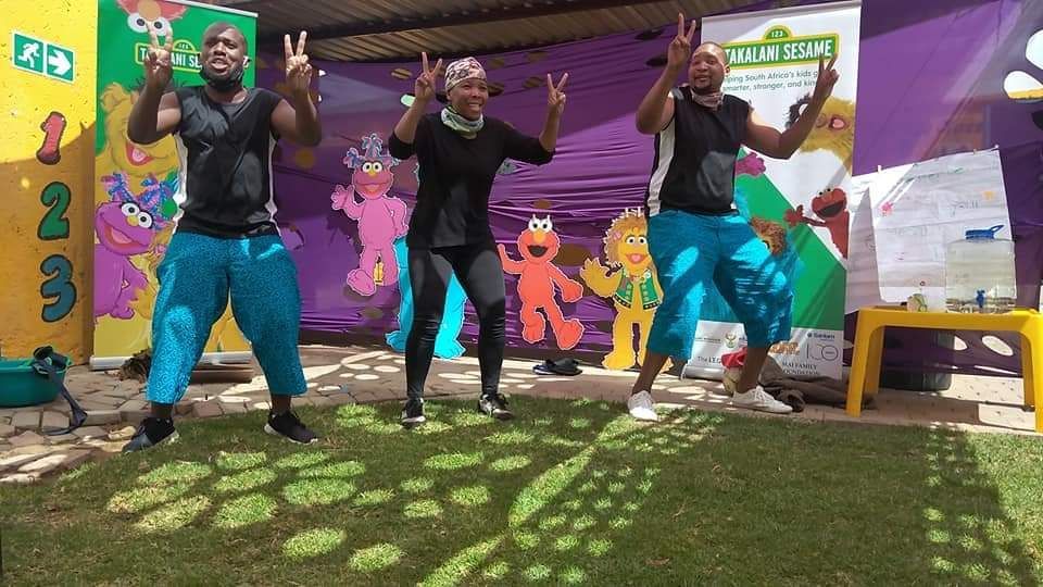 A group of people are dancing in front of a sesame street sign.