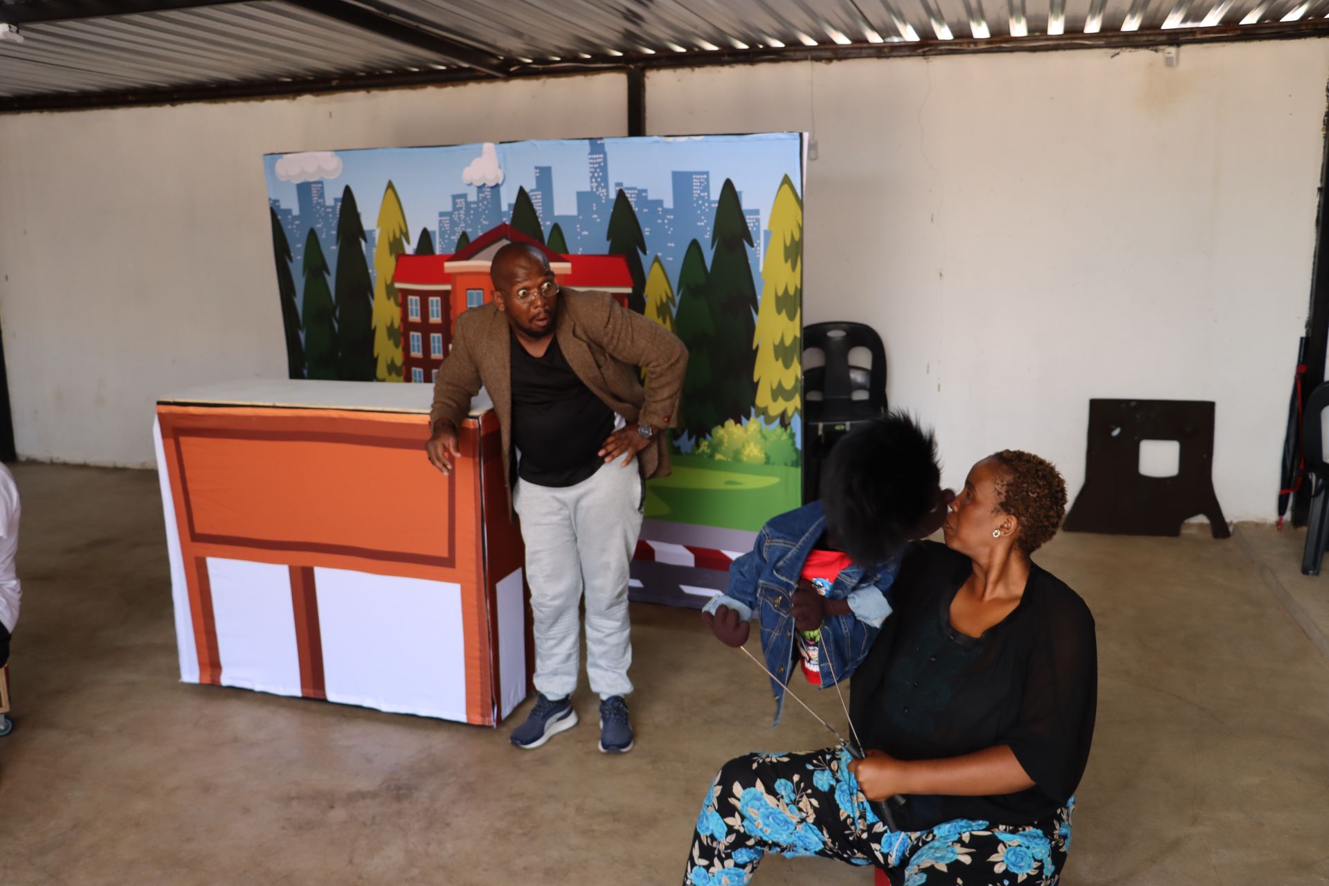 Two women are sitting in front of a cartoon drawing of a building.