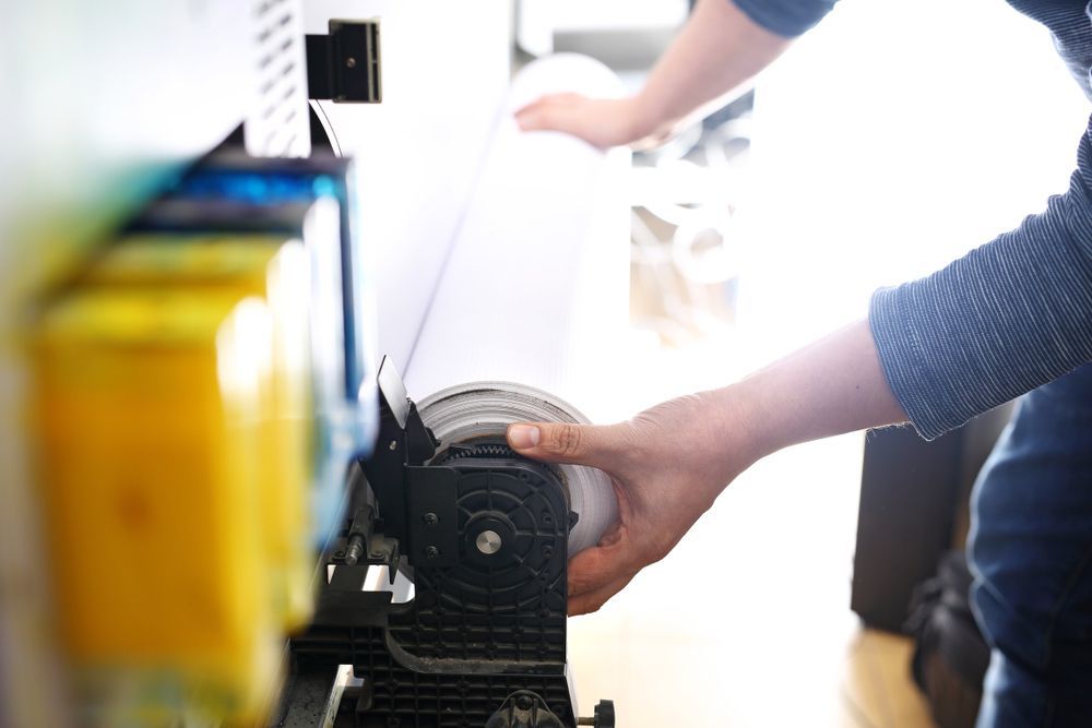 Person is Holding a Roll of Paper in Front of a Printer — Classic Design & Print in Svensson Heights, QLD