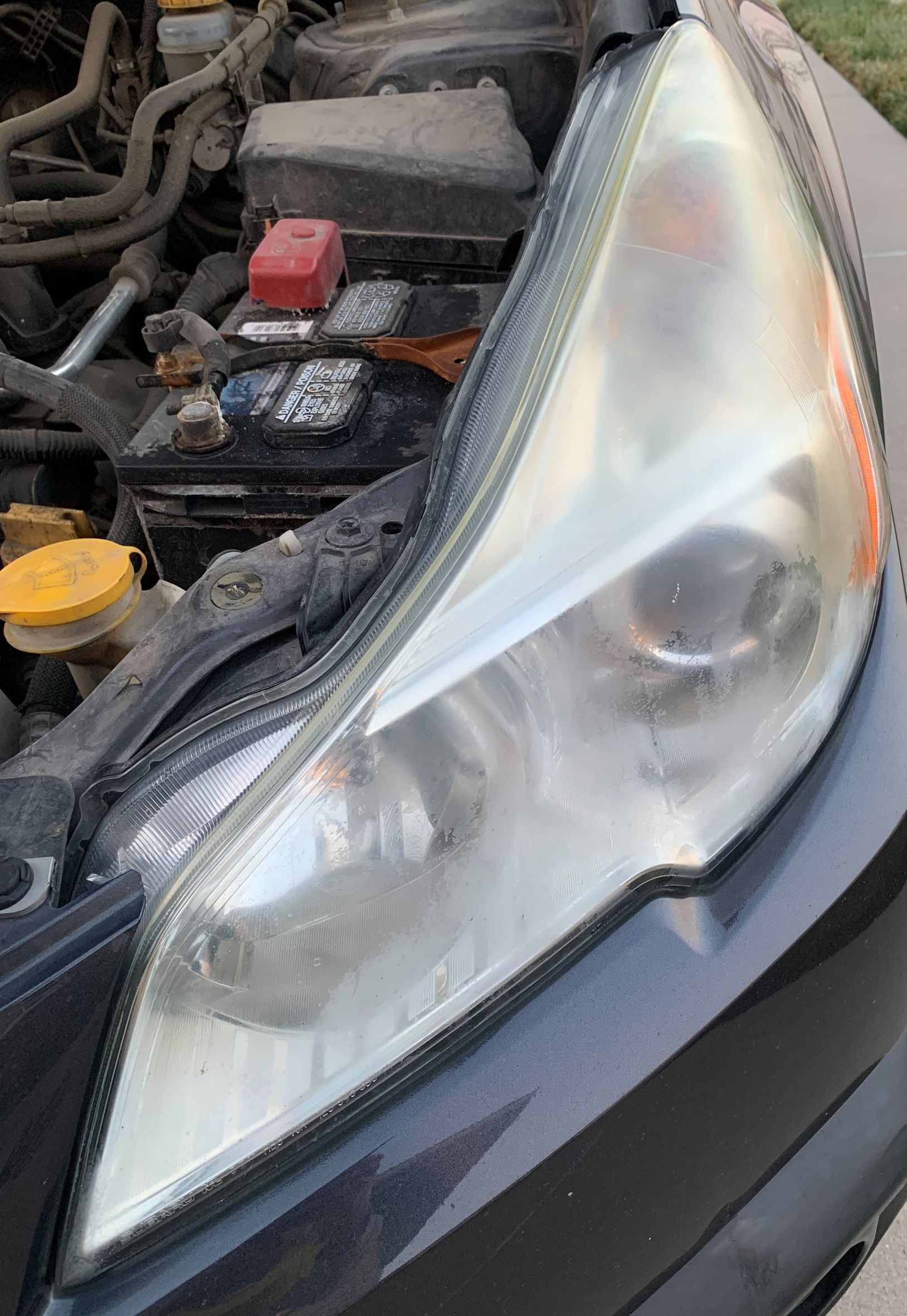 A close up of a car headlight with the hood open.