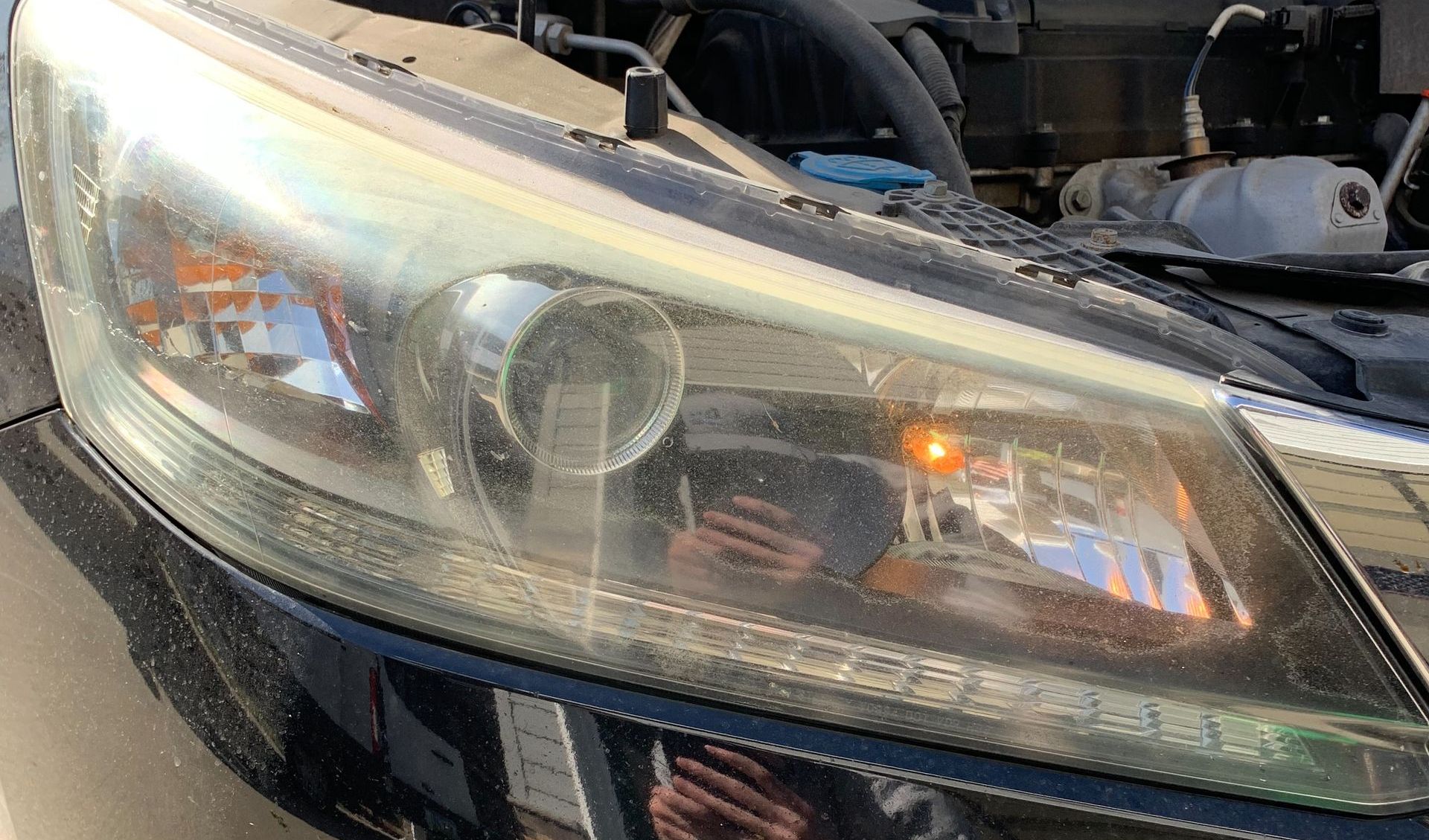 A close up of a car headlight with the hood open.