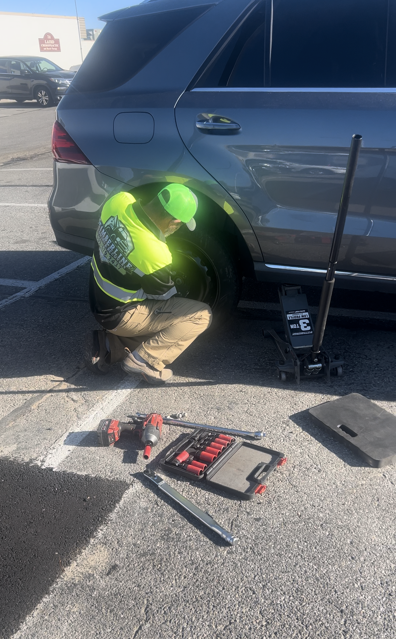 A man is changing a tire on a car in a parking lot.