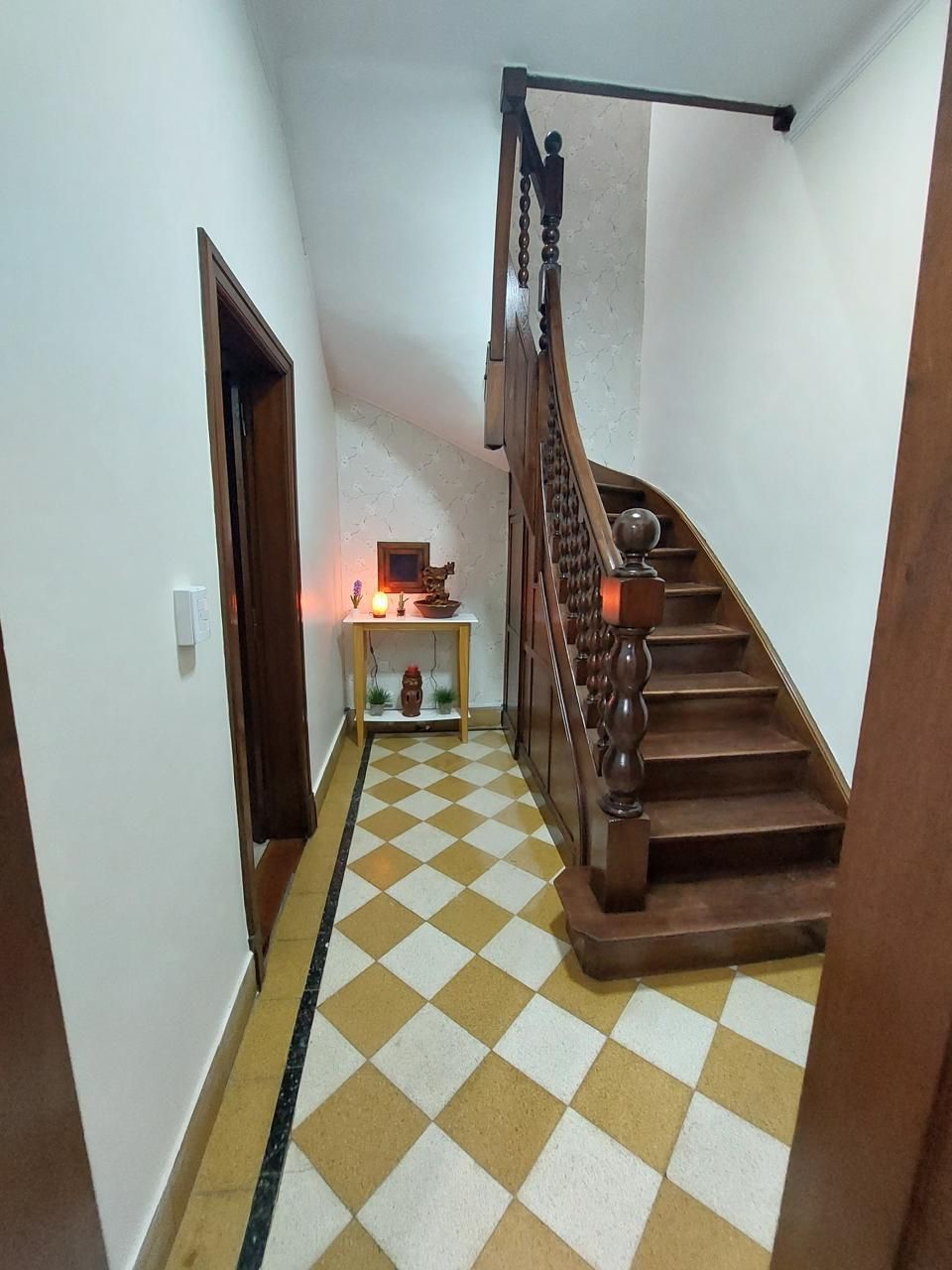 Un pasillo con una escalera de madera y un suelo cuadriculado.