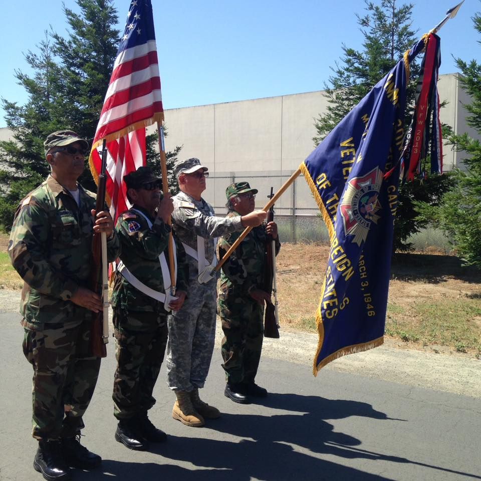 A group of men in military uniforms holding flags one of which says veterans of foreign wars