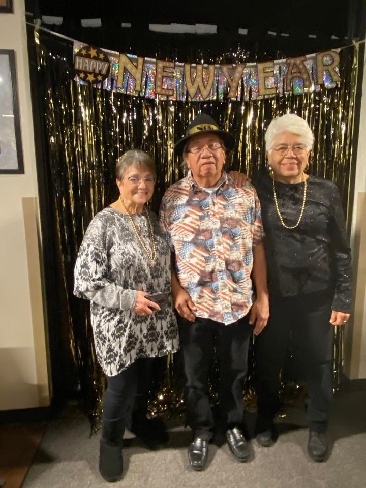 Three people are posing for a picture in front of a new year 's eve banner.