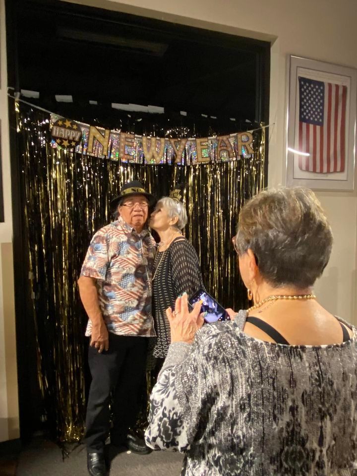 A woman is taking a picture of a man and woman kissing in front of a tinsel curtain.