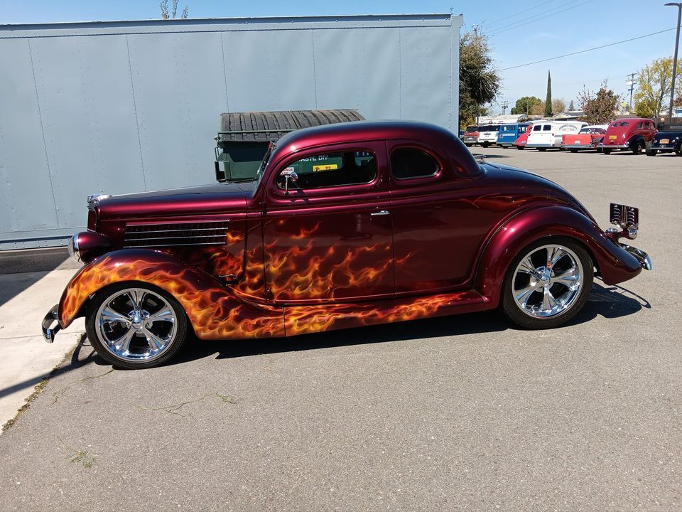 A red car with flames painted on it is parked in a parking lot.