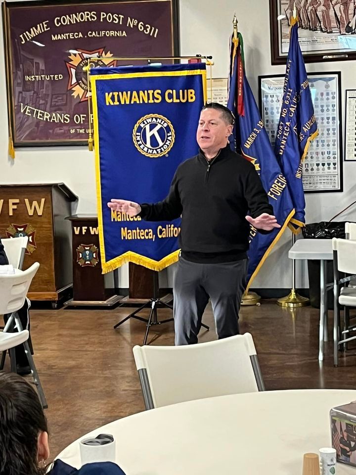 A man is standing in front of a kiwamis club banner.