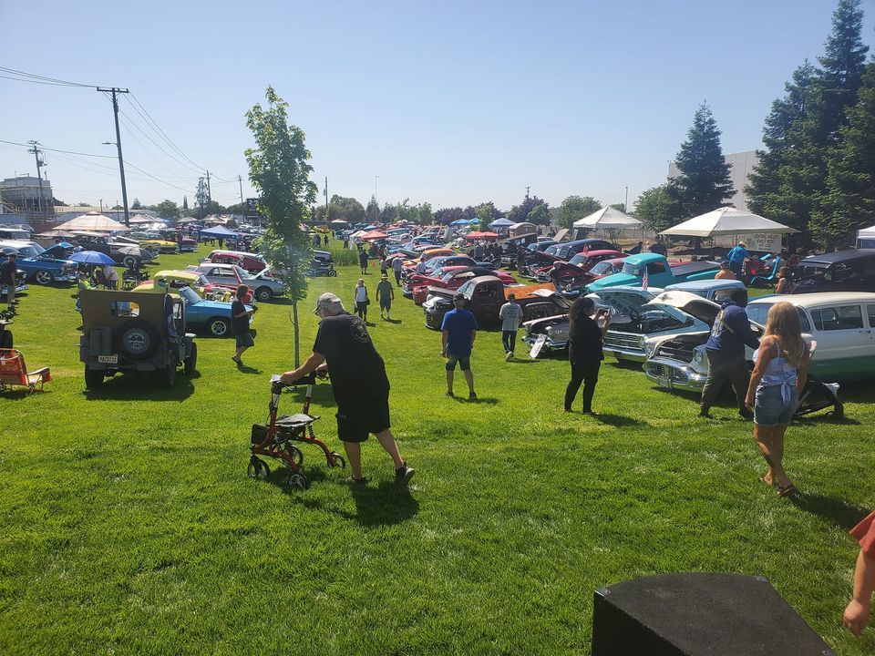 A man with a walker is standing in a grassy field at a car show.