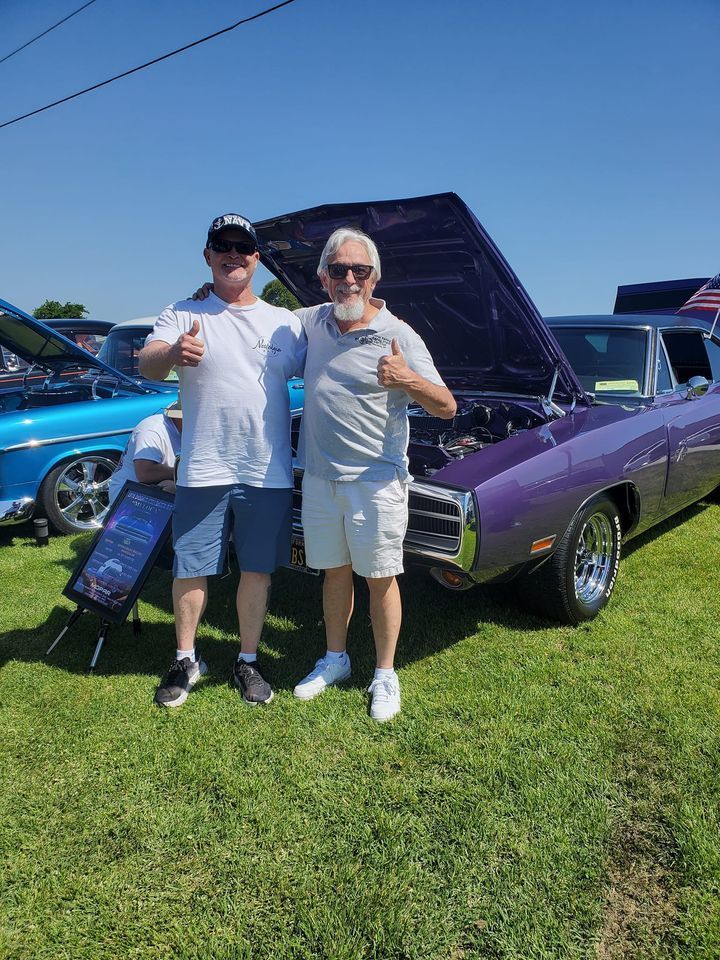 Two men are standing next to a purple car at a car show.