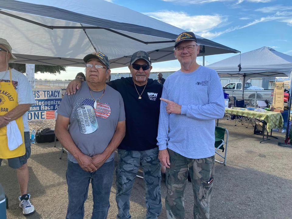 Three men are posing for a picture in front of a tent.