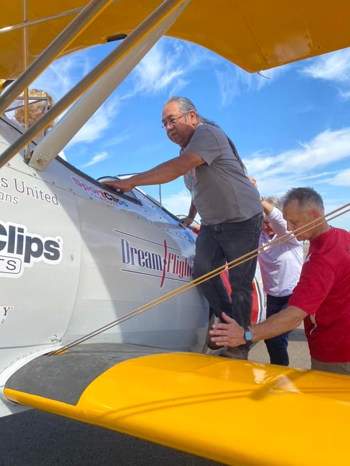 A man in a red shirt is helping another man climb into a plane that says clips on the side